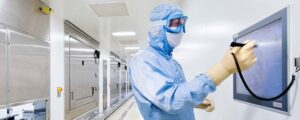 lab worker wearing personal protective uniform and goggles making notes on a monitor